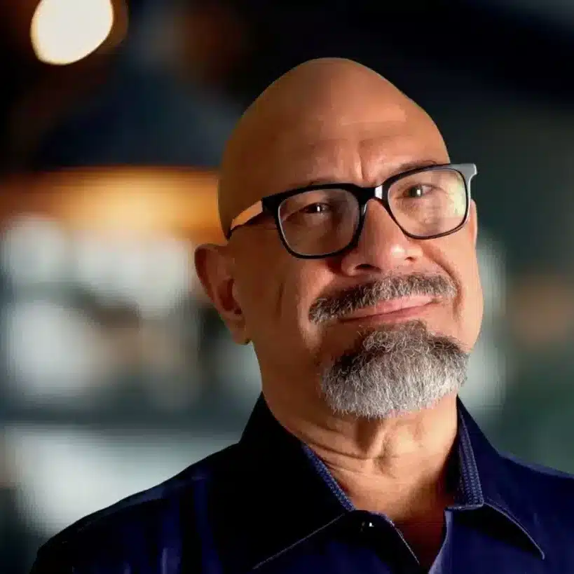 Warm portrait photo of Reynaldo Reyes, smiling Latino man, looking approachable and wise. Soft lighting, blurred warm background.